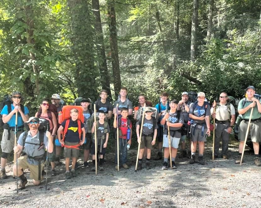 Group of hikers posing with backpacks and trekking poles on a wooded trail.