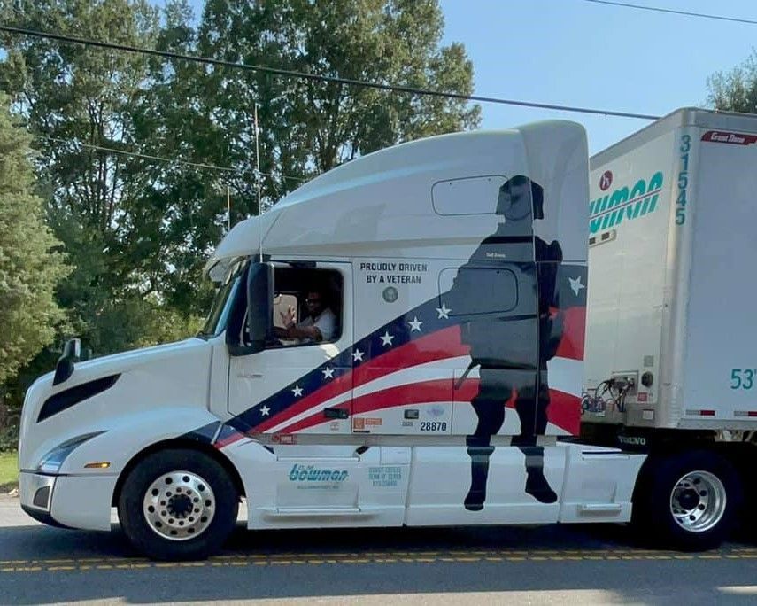 White box truck with a patriotic soldier silhouette and U.S. flag design driving on a road.
