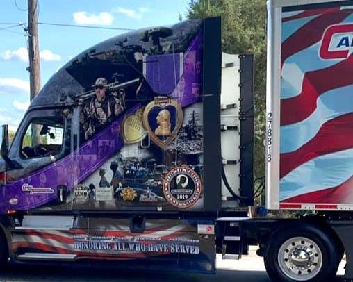 Purple semi-truck with memorial-style graphics and a portrait on the trailer, parked outdoors