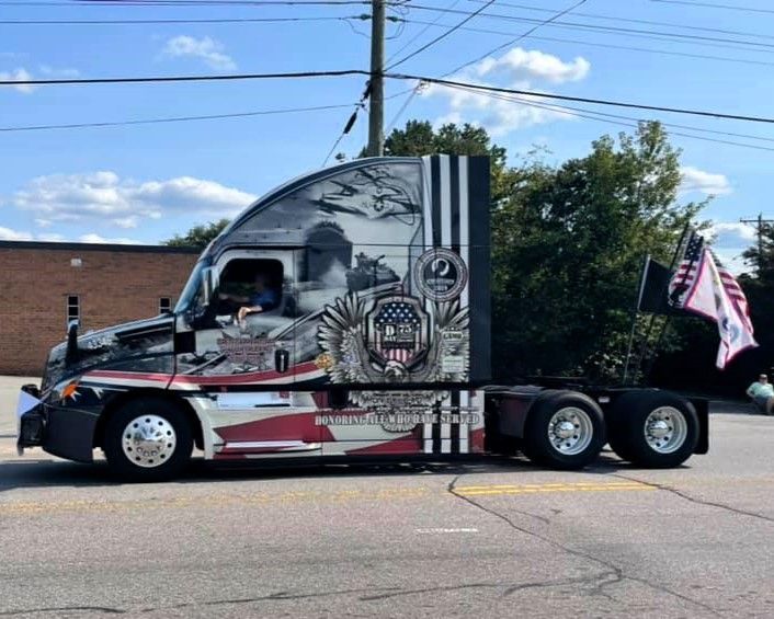 Black semi-truck with a skull mural parked on a street under a blue sky