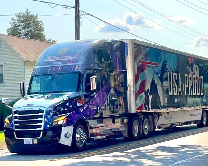 Blue semi-truck with “USA P…” trailer driving on a sunny residential street