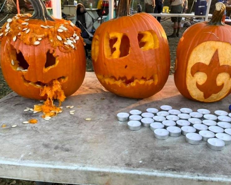 Three carved pumpkins on a table, with silver tea lights and one pumpkin spilling orange pulp.
