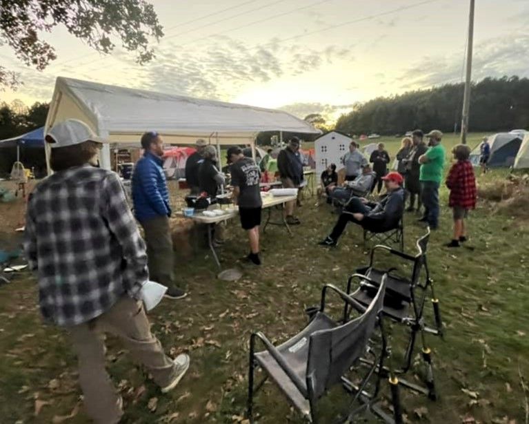 People gathered outdoors around tents and tables at a campsite or community event.