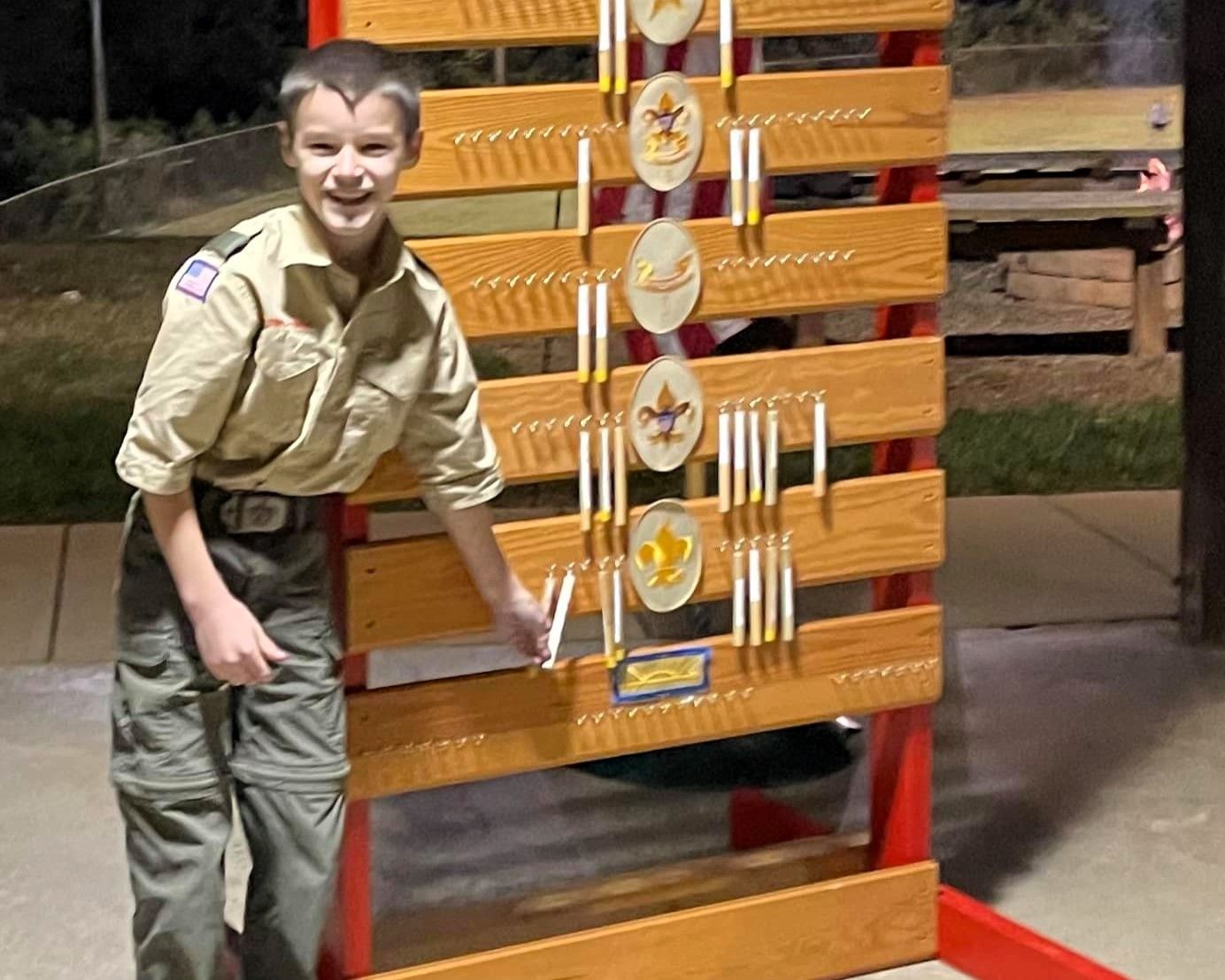 Boy posing beside a large wooden trophy display with medals at an indoor venue.