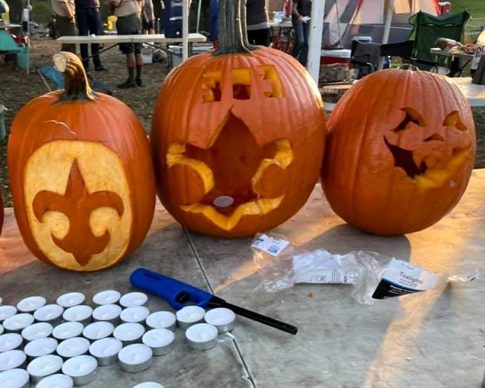 Three carved pumpkins with lit faces and small white tealights on a table outdoors