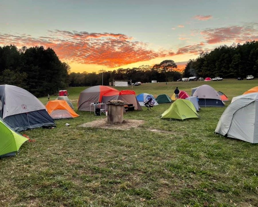 Camping tents on a grassy field at sunset with colorful sky and trees in the background