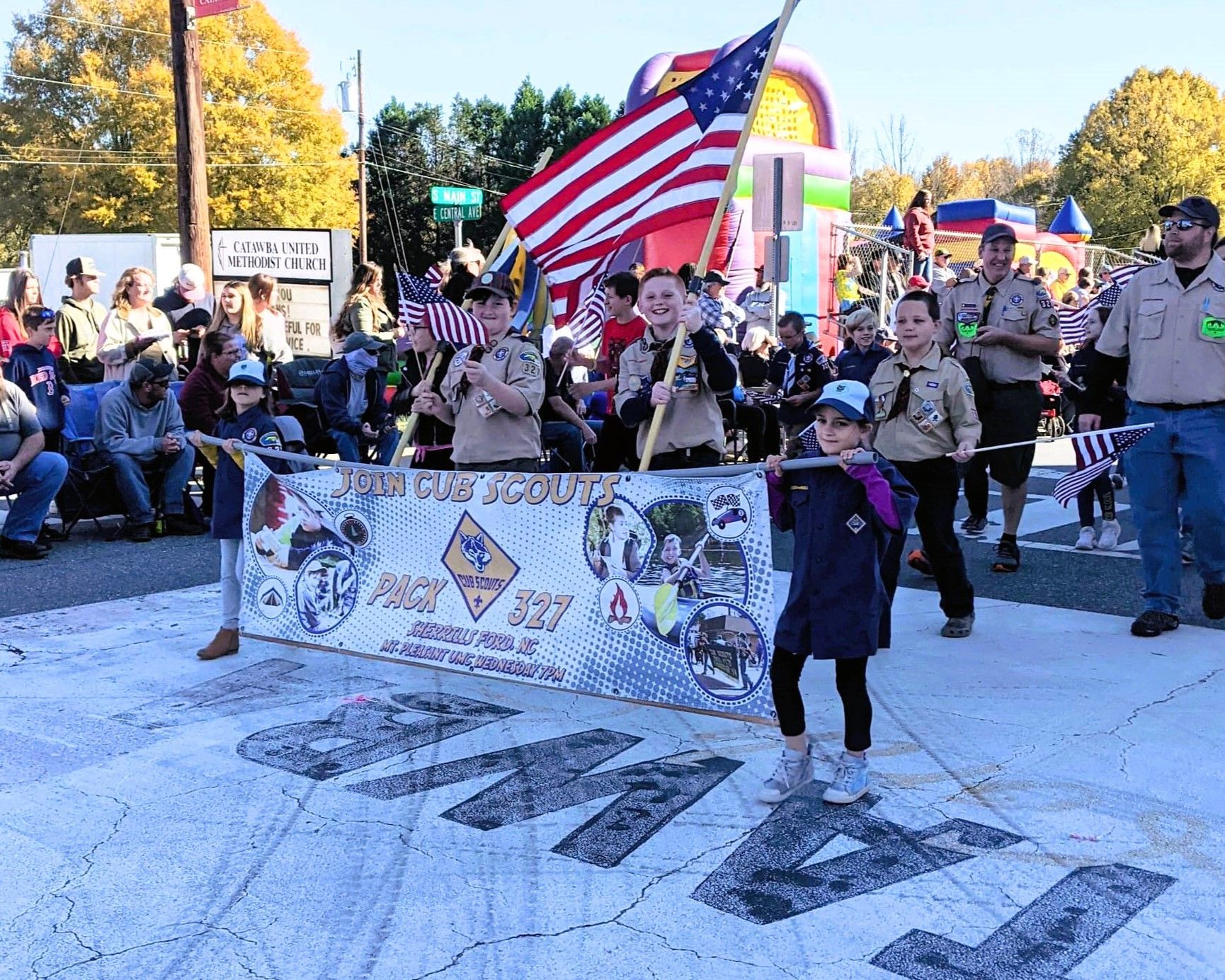 Parade participants holding banners and an American flag on a snowy street, with spectators watching nearby.