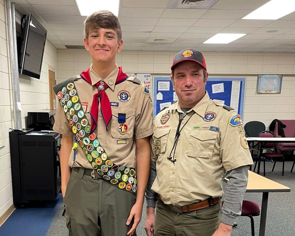 Two Scouts in uniform standing together in a classroom, both smiling at the camera.