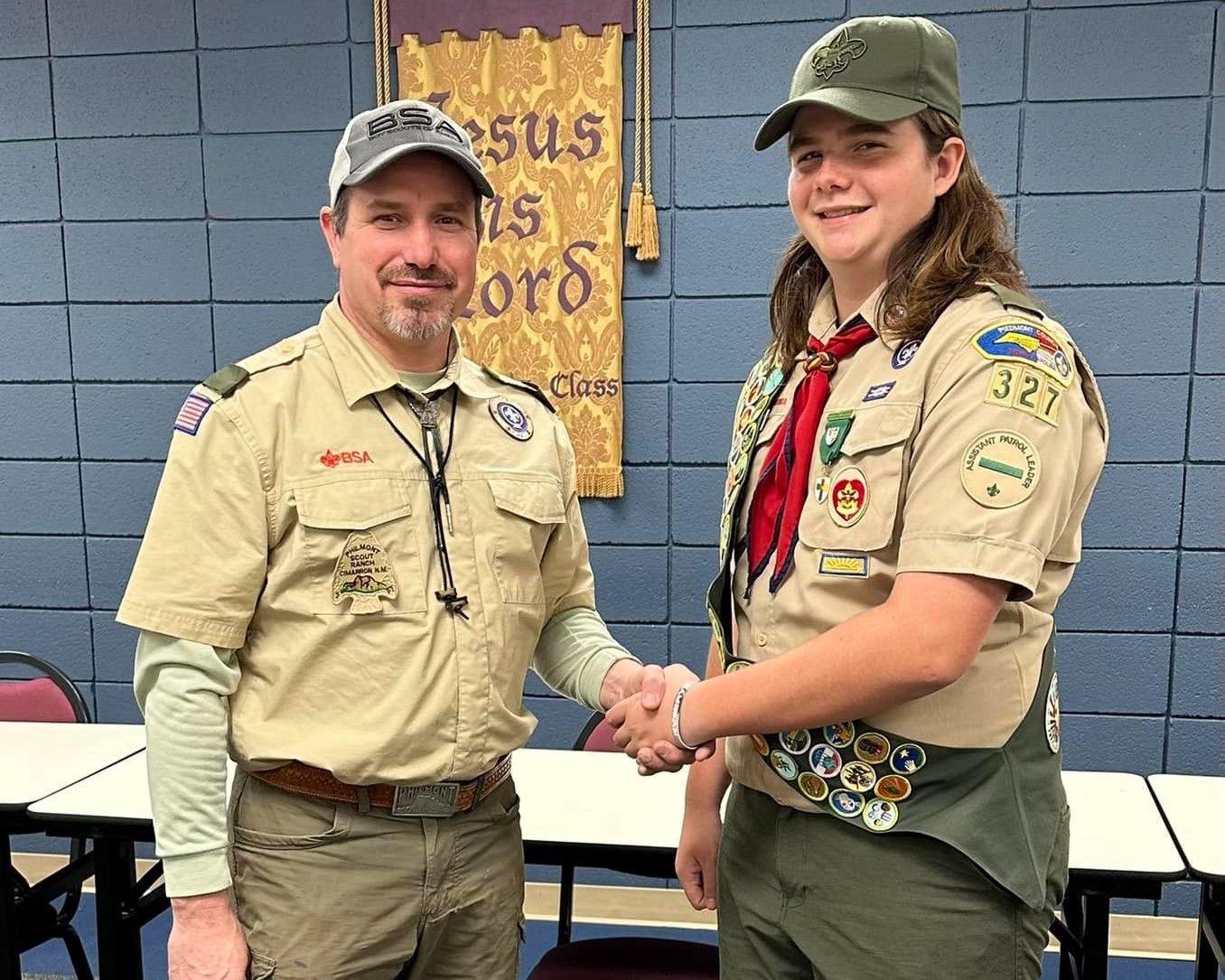 Two scouts in tan uniforms shaking hands in a meeting room