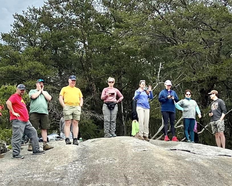 Group of hikers standing on a large rock in a wooded outdoor area