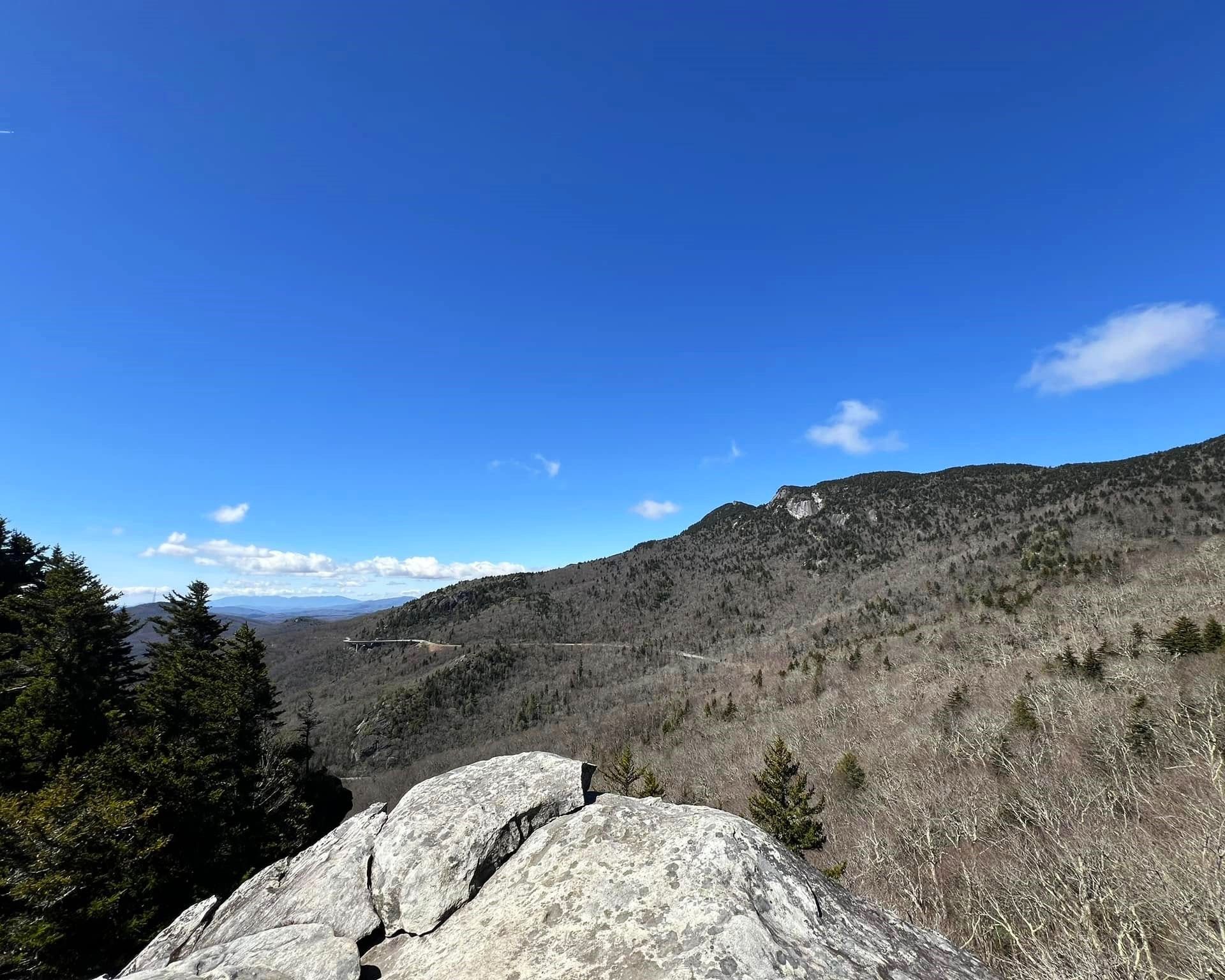 Rocky mountain overlook under a bright blue sky with a distant valley and trees