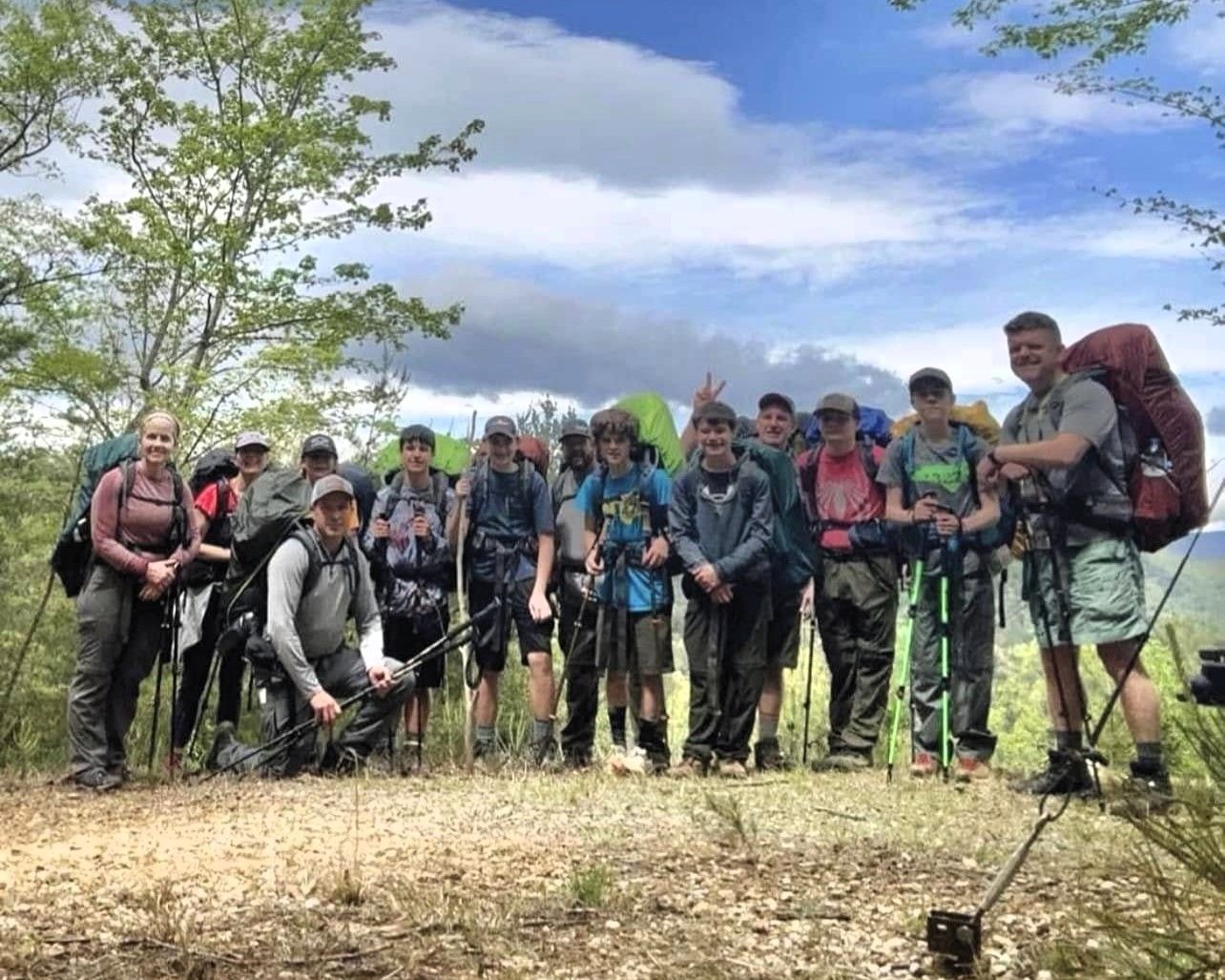 Group of hikers with trekking poles posing on a grassy trail under a blue, cloudy sky