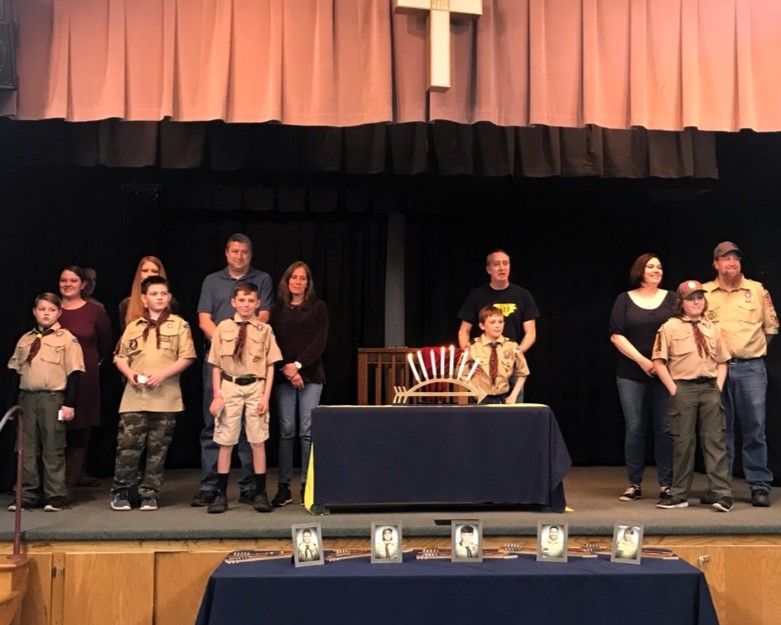 Group of people on a stage around a central table, with curtains behind and awards displayed along the front edge.