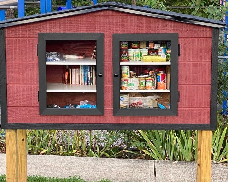 Red little free pantry with books and canned food on wooden legs outdoors