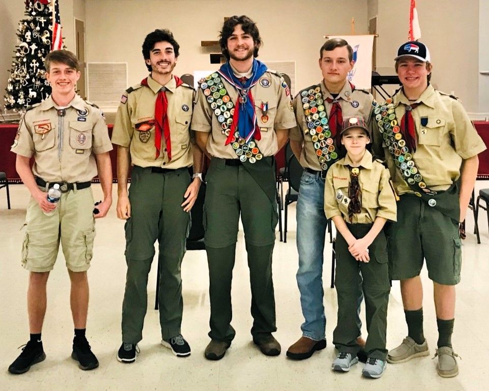 Six scouts in uniforms posing indoors with flags in the background