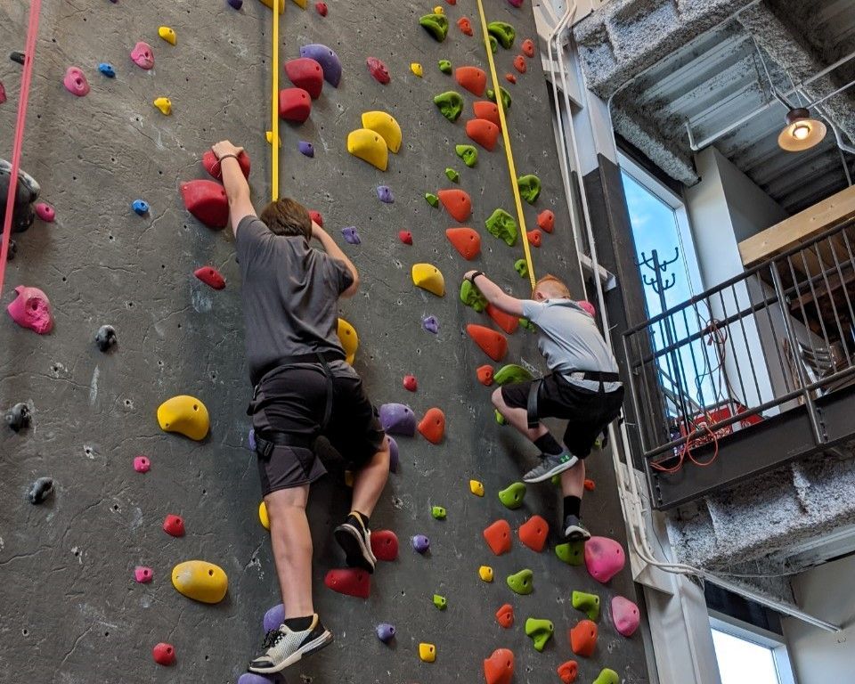 Two climbers on a colorful indoor rock wall, reaching for holds