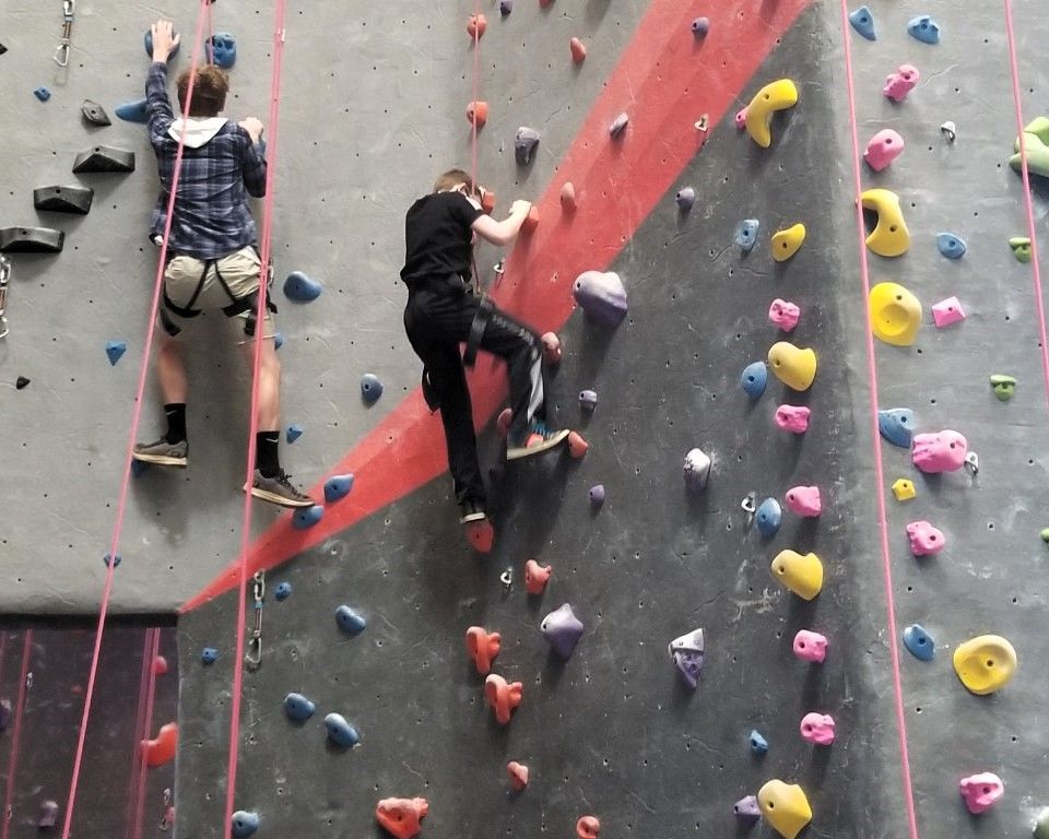 Two climbers on an indoor rock wall with colorful holds and safety harnesses