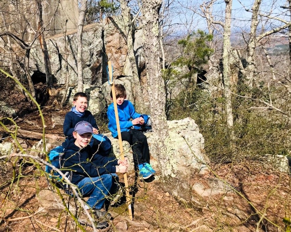 Three hikers in blue jackets resting on rocks in a leafless forest