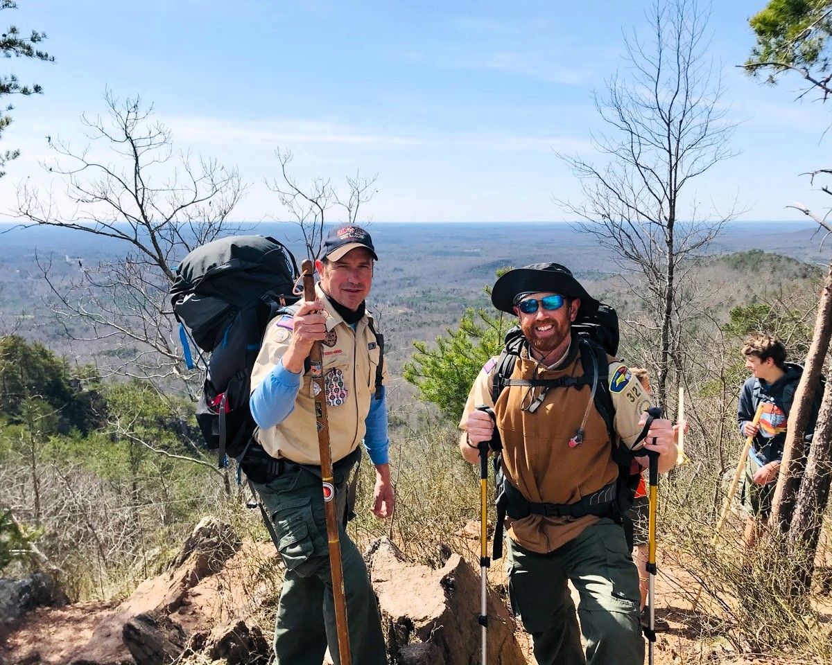Two hikers with backpacks and trekking poles on a sunny mountain trail overlook