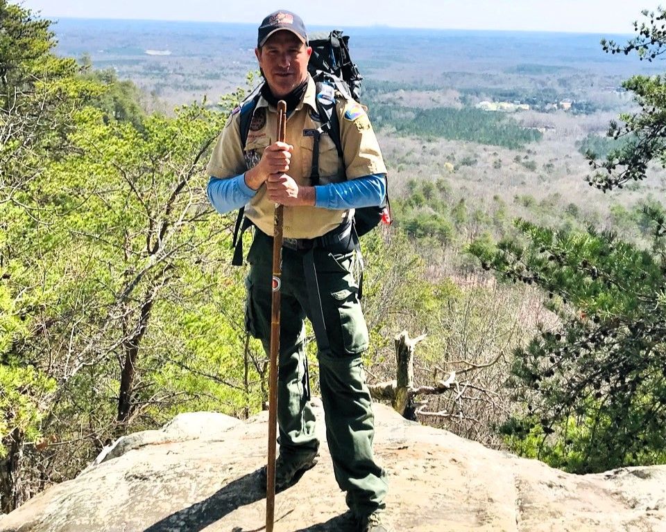 Hiker with trekking poles and backpack standing on a rocky overlook above a forested valley