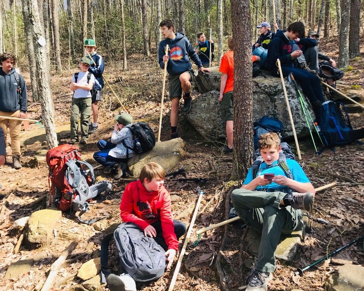 Hikers resting among trees, sitting on rocks and backpacks in a wooded trail area
