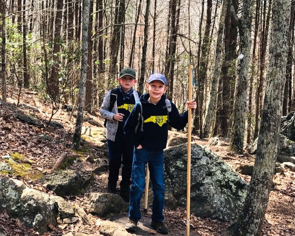 Two hikers with trekking poles on a forest trail among leafless trees and rocks