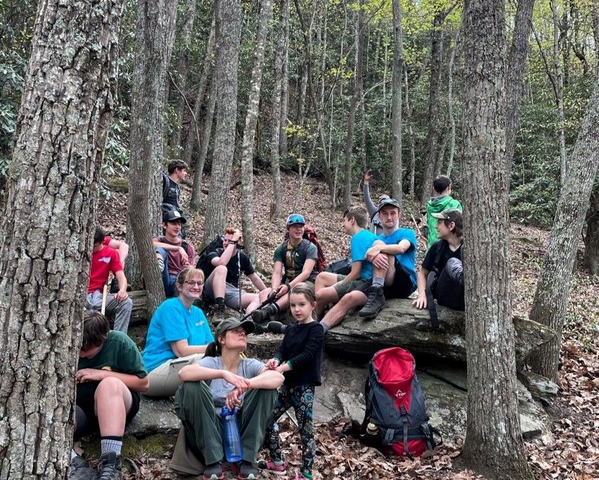 Group of hikers resting on logs in a wooded forest trail