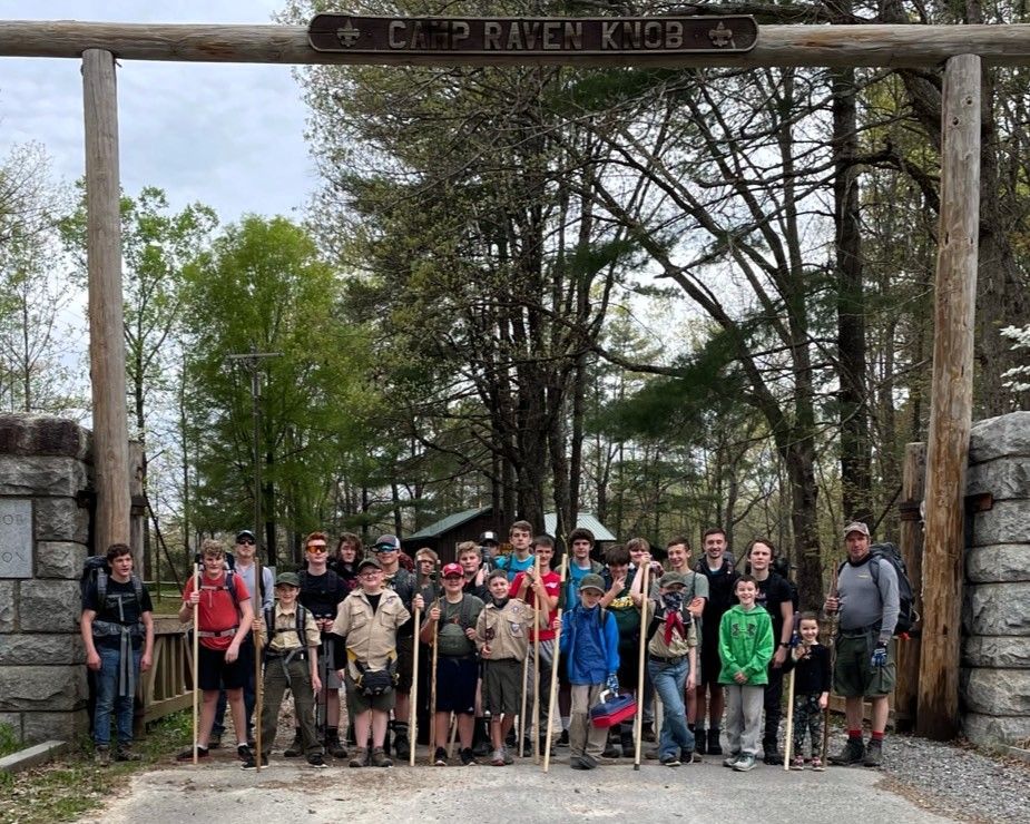Group of hikers posing under a rustic trail sign at a wooded park entrance