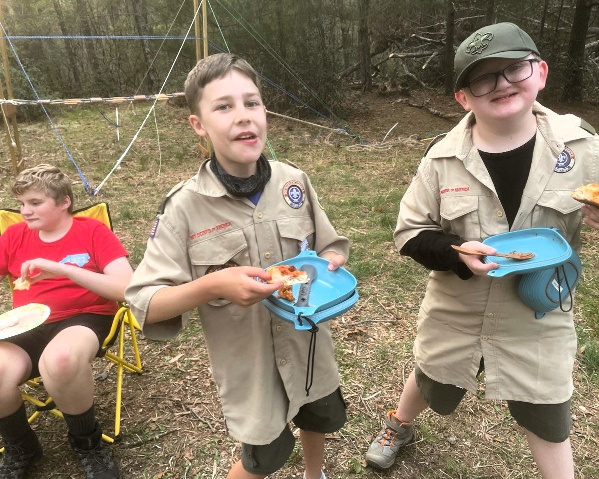 Three children outdoors holding blue devices, two in khaki scout uniforms and one in a red shirt.