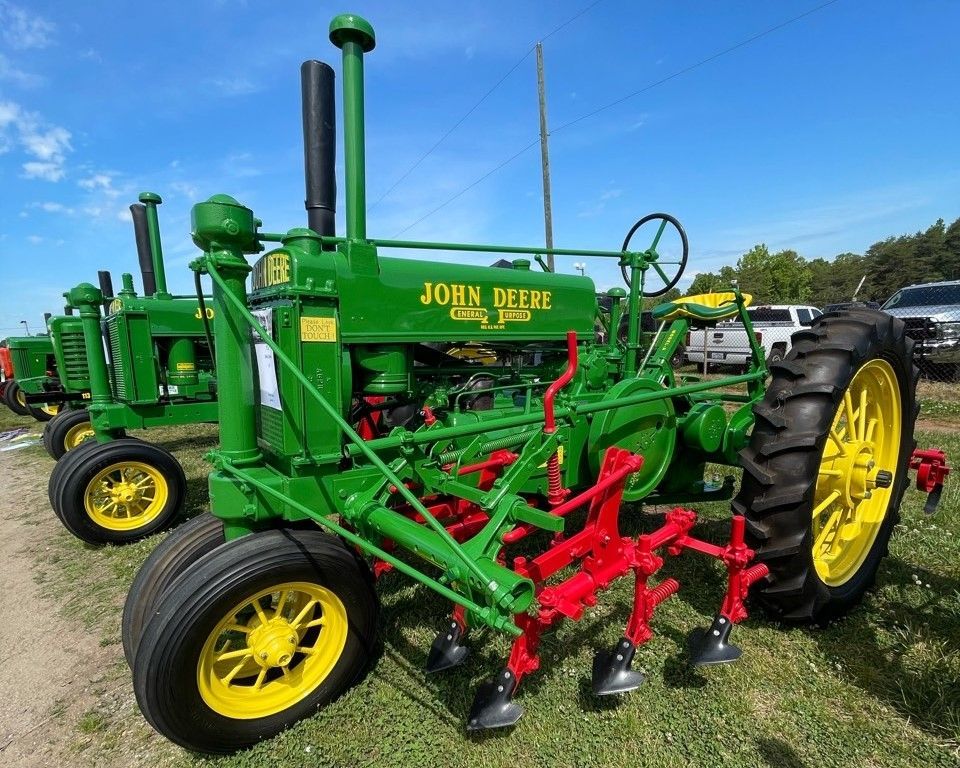Green John Deere tractor with red plow attachments and yellow wheels parked outdoors under a blue sky