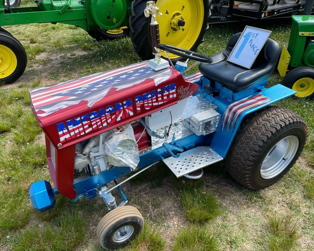 Custom red-and-blue mini tractor with small wheels parked on grass outdoors