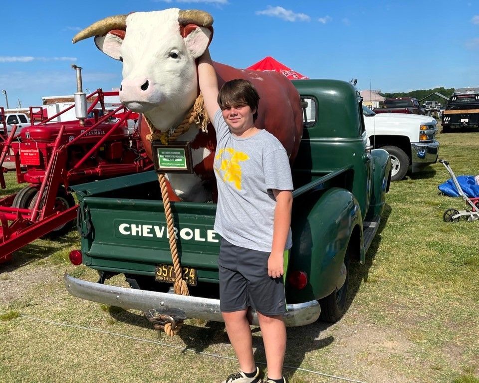 Boy standing beside a vintage green Chevrolet truck with a large bull head display at an outdoor fair