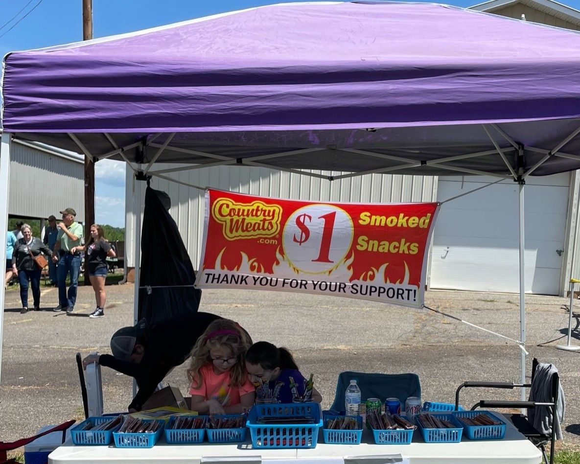Purple-canopy snack stand with a “Smoked Snacks” banner and blue crates on a table at an outdoor market