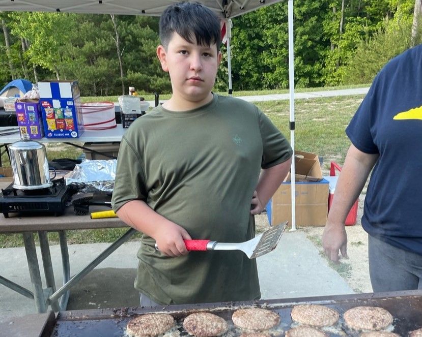Person at an outdoor grill flips burgers with a spatula at a cookout.