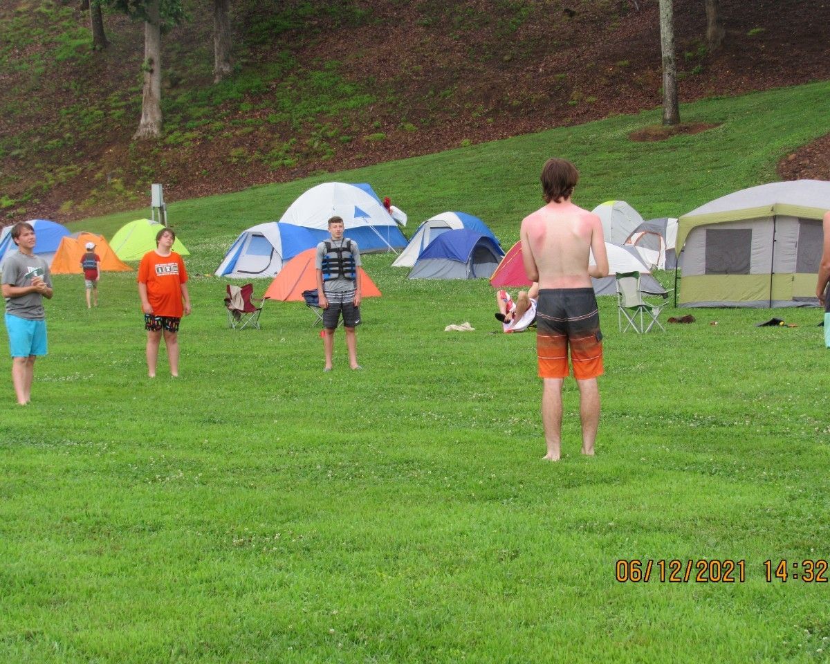 Campers standing on a grassy field with colorful tents in a wooded area.