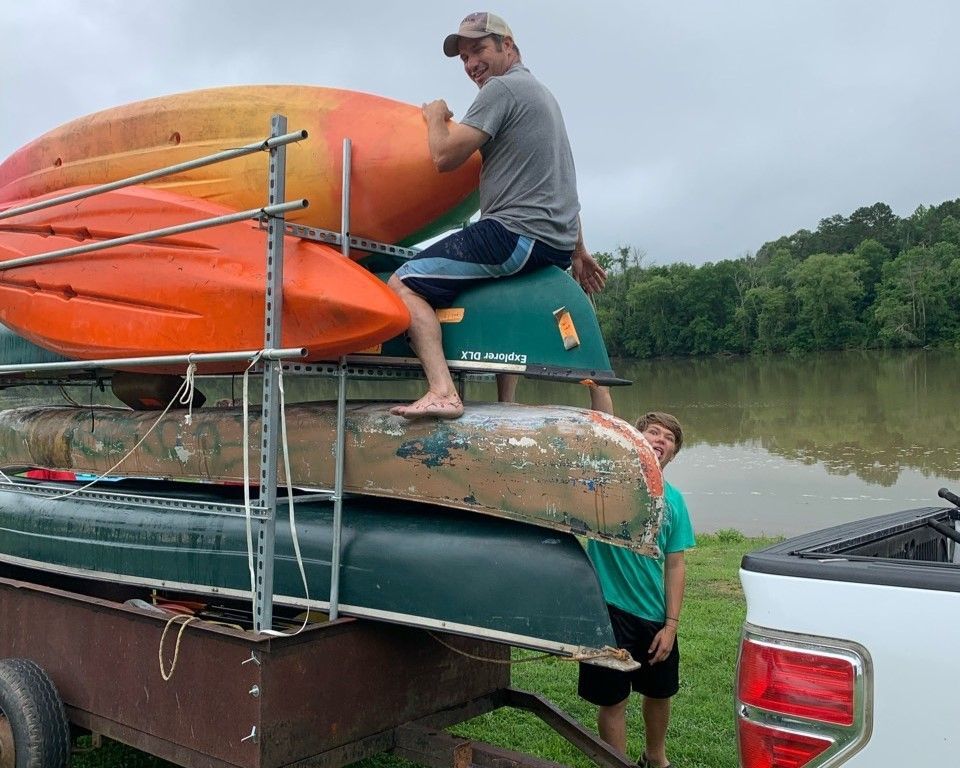 Man loading colorful kayaks onto a truck rack beside a river.