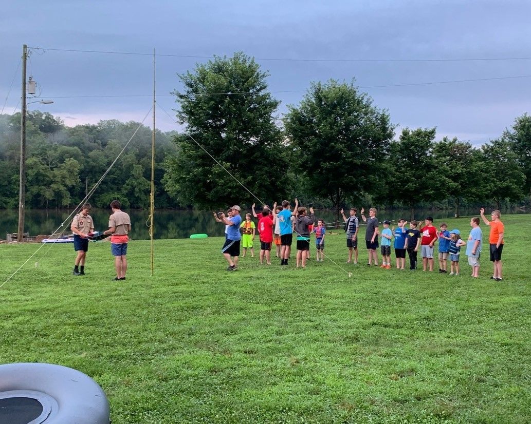 Children gathered on a grassy field outdoors, standing in a loose group near volleyball poles.