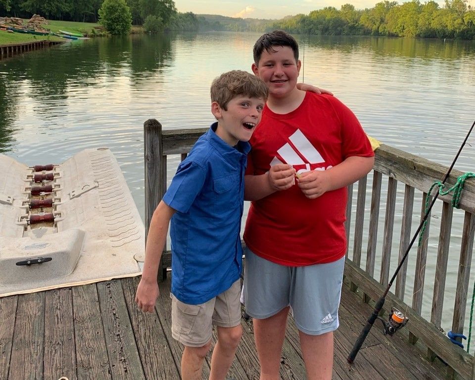 Two people standing on a dock by a calm lake, smiling and posing together.