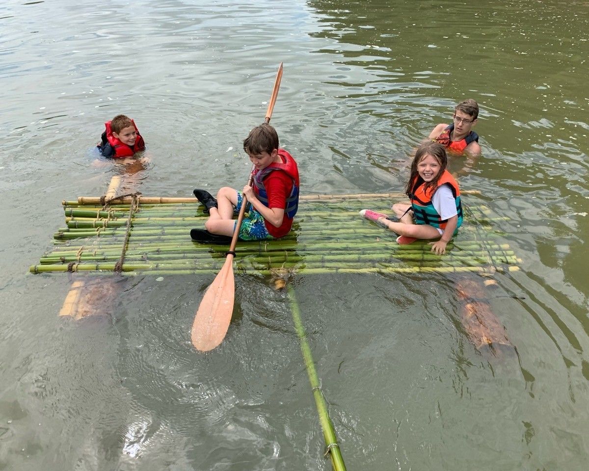 Children in life jackets paddling a bamboo raft on calm water