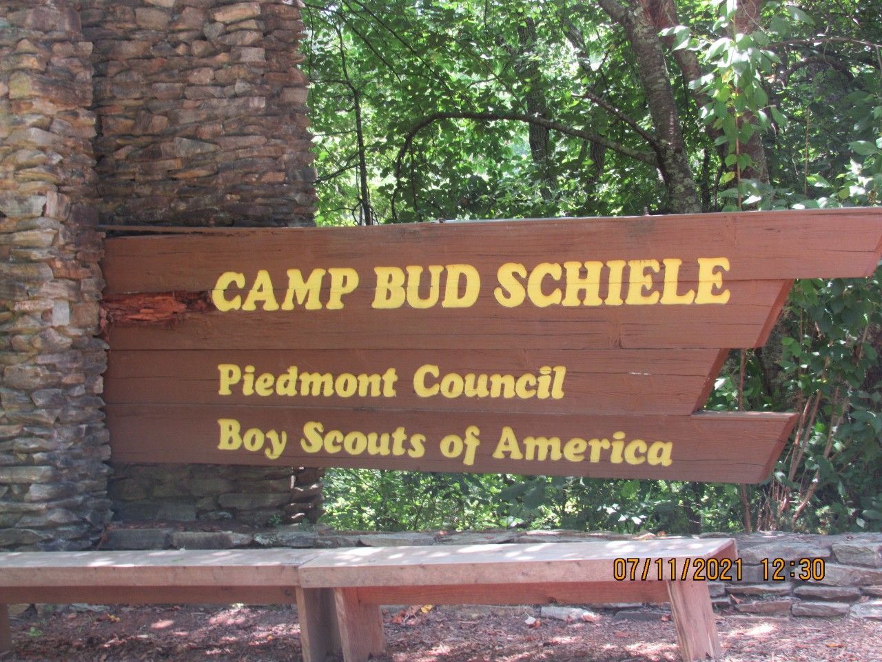 Wooden sign reading “Camp Bud Schiele” for Piedmont Council Boy Scouts of America among trees