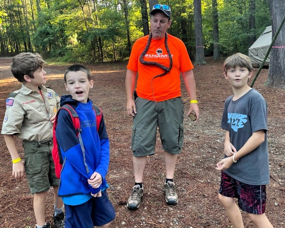Four children and an adult stand on a wooded trail, wearing casual hiking clothes.