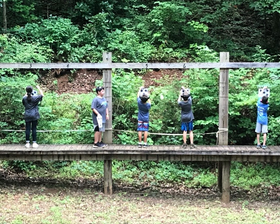 Five people on a wooden platform outdoors, holding cameras or phones in a forest setting.
