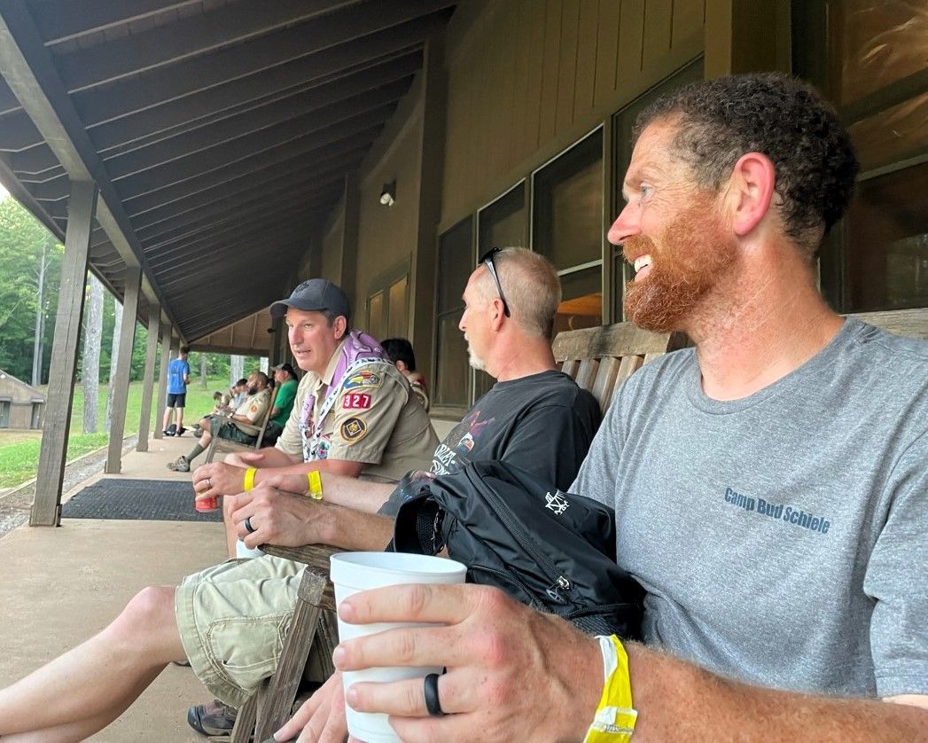 People seated on a covered porch, smiling and chatting, with drinks in hand.