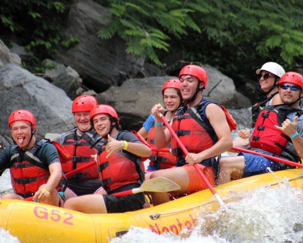 Rafting team in red helmets paddles through whitewater in a yellow inflatable raft