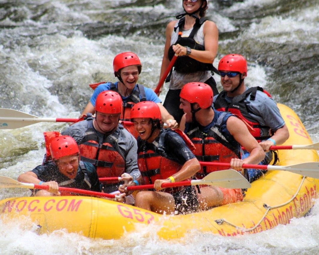Six people in red helmets whitewater rafting through rough rapids in a yellow raft