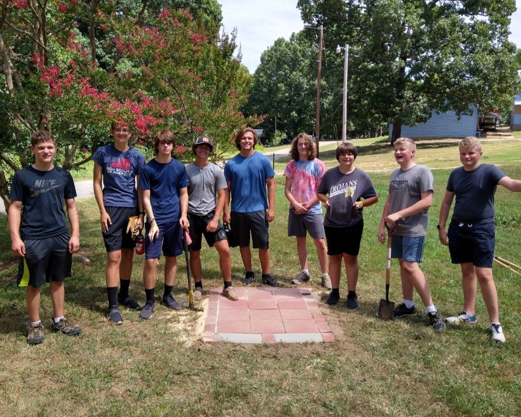 Group of people posing outdoors on a sunny day beside a red concrete pad and trees