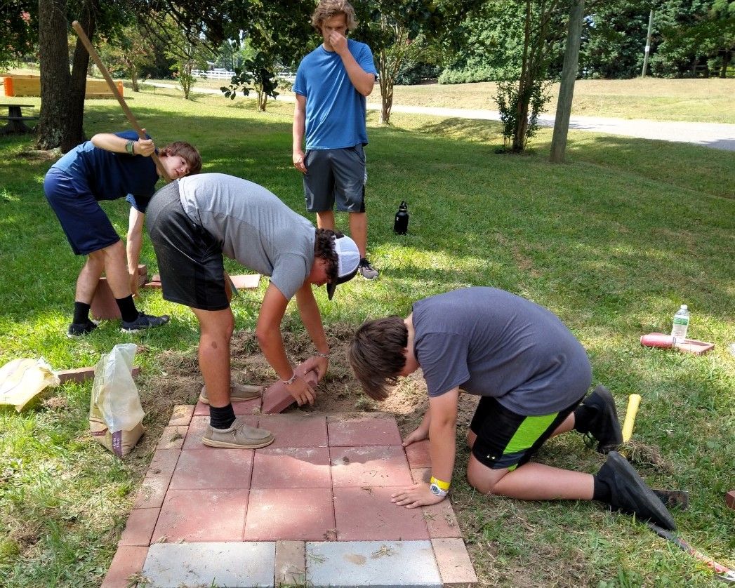People kneeling outdoors, planting or arranging pavers in a grassy yard.