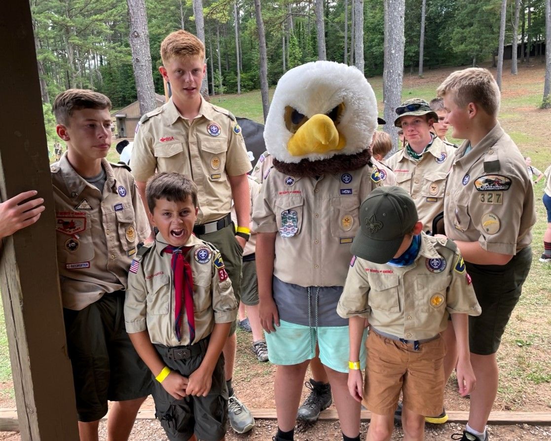 Boy Scouts standing with an eagle mascot in a wooded outdoor setting.