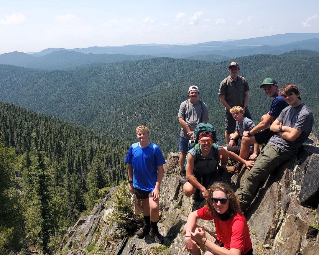 Group of hikers resting on a rocky mountain overlook above a forested valley