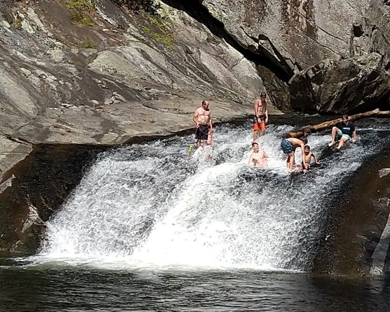 People sliding and swimming over a small waterfall between dark rock walls
